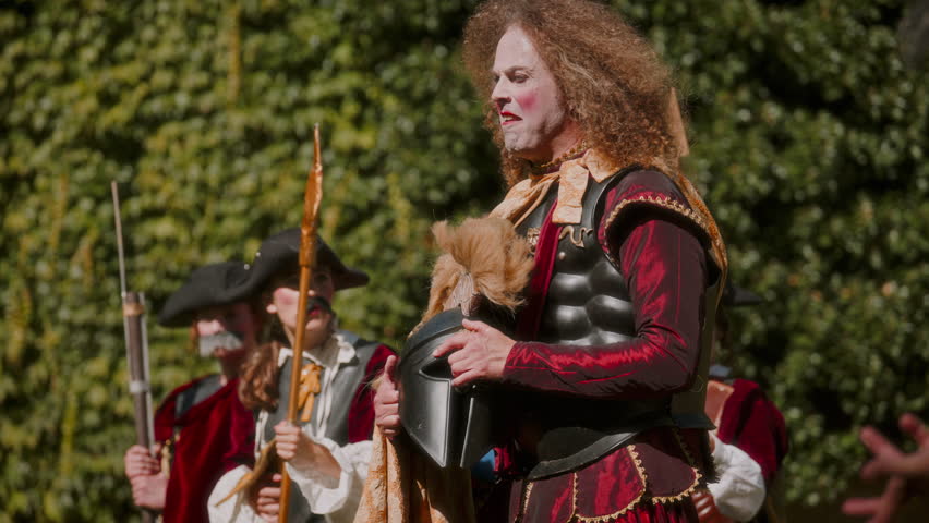 A commanding general flanked by a group of footmen wielding spears in a theatrical performance outdoors