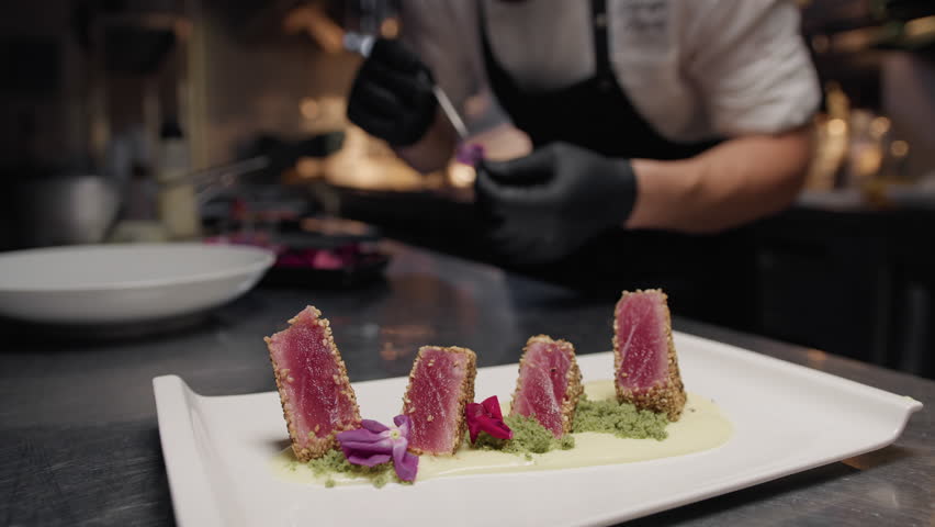 Chef Is decorating with flowers tuna fish fillets for second course in kitchen