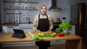 Vlogger woman chef with headscarf in an apron recording video cooking lesson about vegetarian meal or salad in modern kitchen at home. Online broadcast, woman leads food blog or course