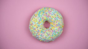Delicious sweet donut rotating on a plate. Top view. Bright and colorful sprinkled donut close-up macro shot spinning on a pink background.