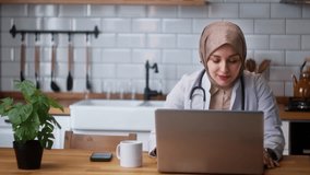 Young female doctor in headscarf wears white coat talking to patient using virtual chat computer app. Remote healthcare services concept