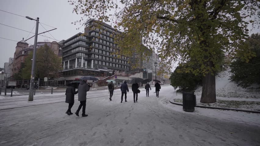 people walking with umbrelas on snowy roads in oslo in slow motion