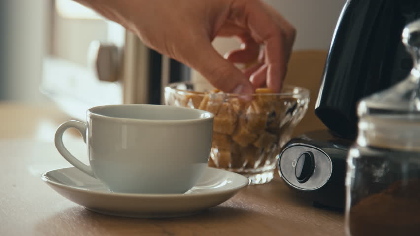 Side stab closeup of hand adding one brown sugar lump to cup of coffee or tea and dissolving it with teaspoon in modern kitchen Royalty-Free Stock Footage #3403806953