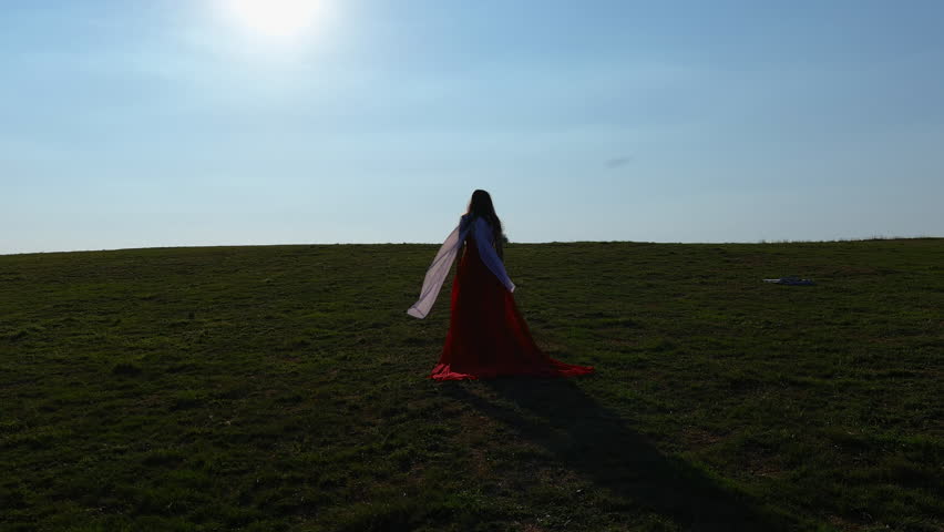 A Woman in a Long Red Dress and a White Scarf Walking Towards the Horizon