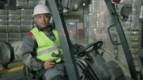 Portrait of male beverage storehouse worker in helmet and vest sitting in loading machine and looking at camera - Powered by Shutterstock - Get 15% off with code: PIKWIZARD15