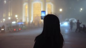 tourist woman shooting video in city at night with blurred traffic as background