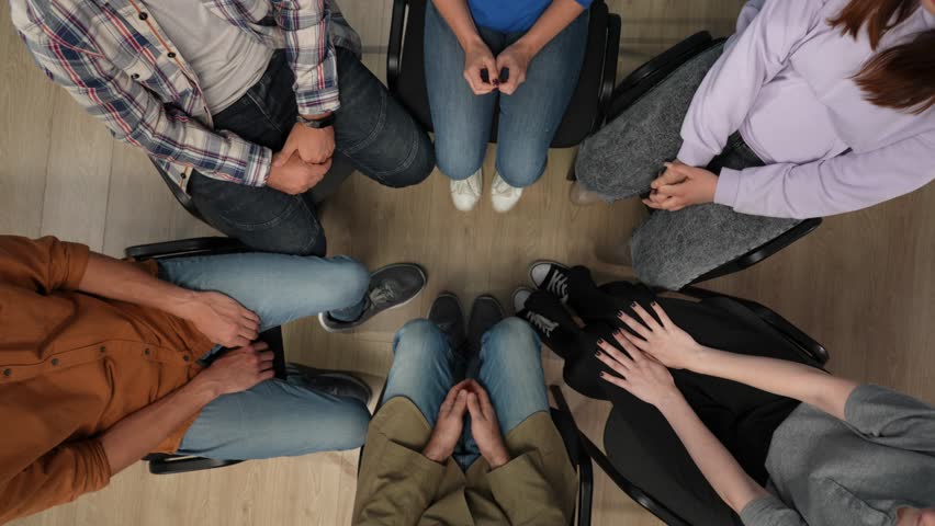 Close up of a group of people sitting in a circle in the frame above. They have come for a therapy session with a psychologist, they are socializing, working through problems, supporting each other Royalty-Free Stock Footage #3404066859