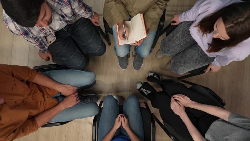 In the shot above is a close up of a group of people. They have come for a therapy session with a psychologist, talking about their problems, the doctor is taking notes in a notebook. Then disperse Royalty-Free Stock Footage #3404067665