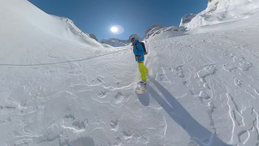 SELFIE, LENS FLARE: Male splitboarder carving down the untouched snowy mountain. An incredible landscape in a high alpine world with an extreme snowboarder enjoying every turn on fresh powdery snow. Royalty-Free Stock Footage #3404190649