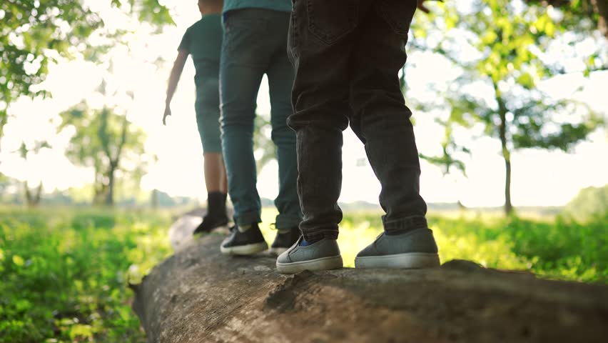 baby boy group playing in the forest park. close-up child feet walking on fallen tree log. happy family kid dream concept. a child group in sneakers lifestyle walks on a fallen tree in park