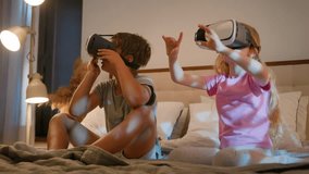 Funny little amazed caucasian children kids boy girl brother sister playing video game using digital virtual reality headset play online metaverse 3d with VR glasses in bedroom innovative technology