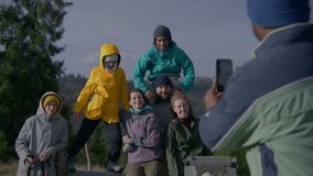 African American man takes group photo of his multiethnic friends on the top of hill against scenic view using phone. Diverse hiking buddies on vacation trip or trek in mountains. Tourism and travel. - Powered by Shutterstock - Get 15% off with code: PIKWIZARD15