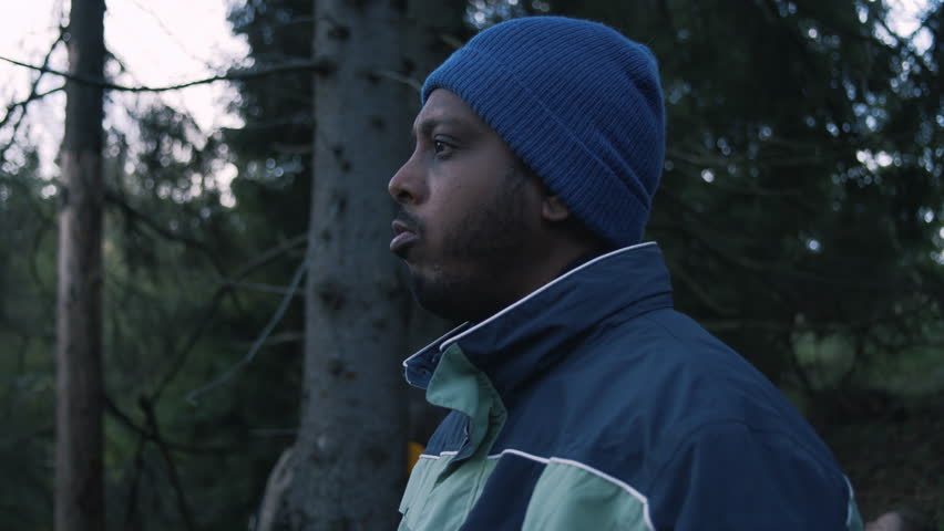 African American man having snack in the woods during tourist trip or trek in autumn. Adult hiker or traveler resting in camp after long hike in the mountains. Tourism and travel concept. Slow motion.