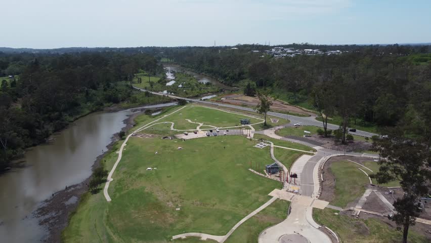 Drone flying over a recreational park towards a river with bridge where cars are passing by