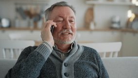 Positive senior man calls phone at home. Portrait old gray haired male talking on smartphone sitting on couch, smiling laughing enjoying conversation with friend, relative. Happy sociable person. - Powered by Shutterstock - Get 15% off with code: PIKWIZARD15