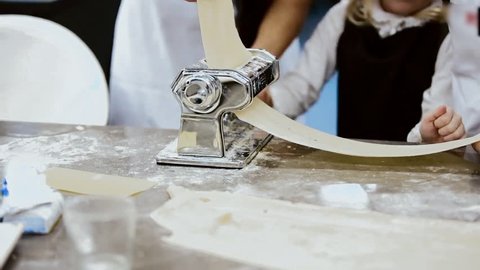 children with their grandmother make sheets of pasta for lasagna. homemade pasta for lasagna on a home machine for lasagna. Making Lasagna sheets at home, flattened dough in pasta machine close-up