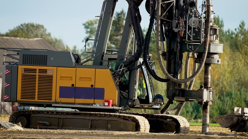 Machine lowers drill down. Drilling water wells. Digs holes in ground with drilling rig. Equipment for installing piles in ground heavy machines. Driving pillars work in laying foundation building