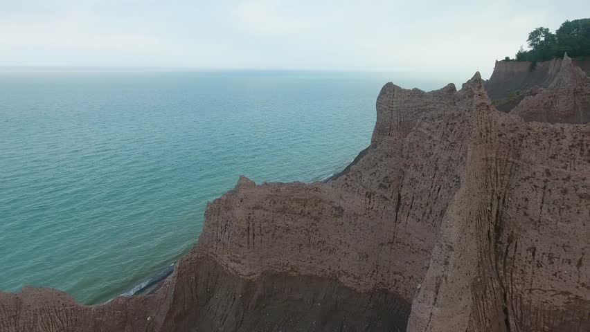A 4K drone shot over the large clay formations of Chimney Bluffs State Park, on the water