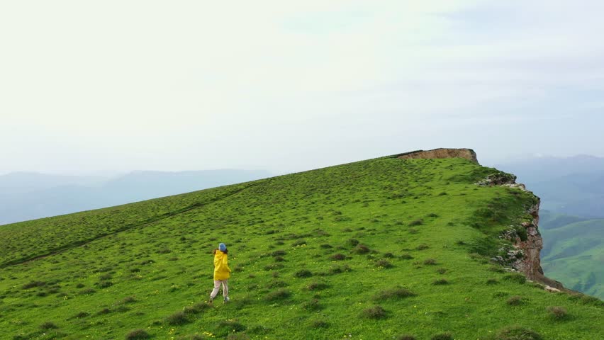Young woman running along the rocky cliff edge. Aerial view of scenic rocky cliff. Mayak mountain in Gunib region, Dagestan