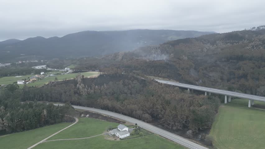 Aerial view of highway going through smoky burnt and green eucalyptus forest and mountains under cloudy sky