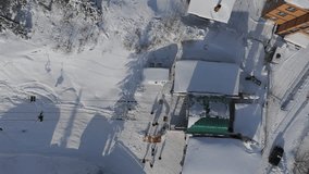 Aerial: top down to the bottom station of the chairlift. Skiers sit in chairs. Sheregesh