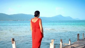 Beautiful woman walking down pier in long red dress. Phu Quoc Island. Landscape of mountains and sea. The woman walks on a pier on the island. Slow mothion
