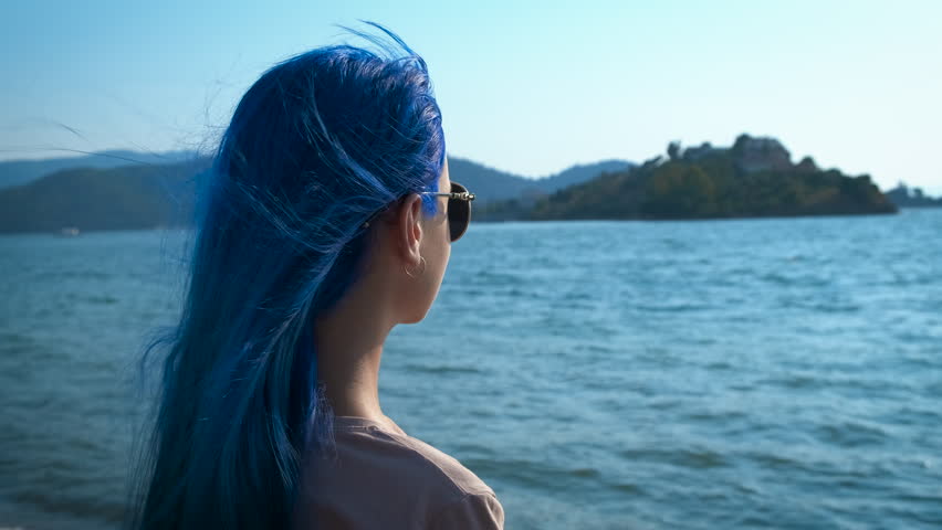 Hair in the color of the sea. A girl with blue hair looks at the seascape.