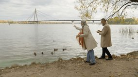 Senior couple woman man near lake throwing bread feeding ducks together middle aged old family romantic walk in autumn park outdoors retired grandpa grandma female male feed birds floating in river - Powered by Shutterstock - Get 15% off with code: PIKWIZARD15