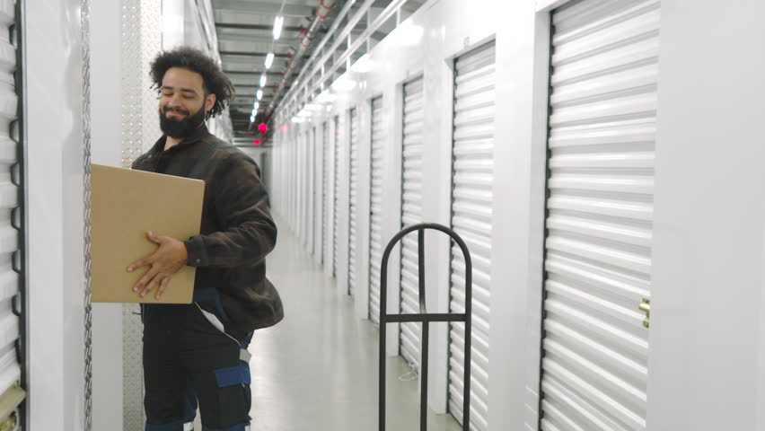 African American in work overalls lifting heavy boxes with items of customer, employee touching lower back feeling pain. Loader in self storage company. High quality 4k footage Royalty-Free Stock Footage #3404972921