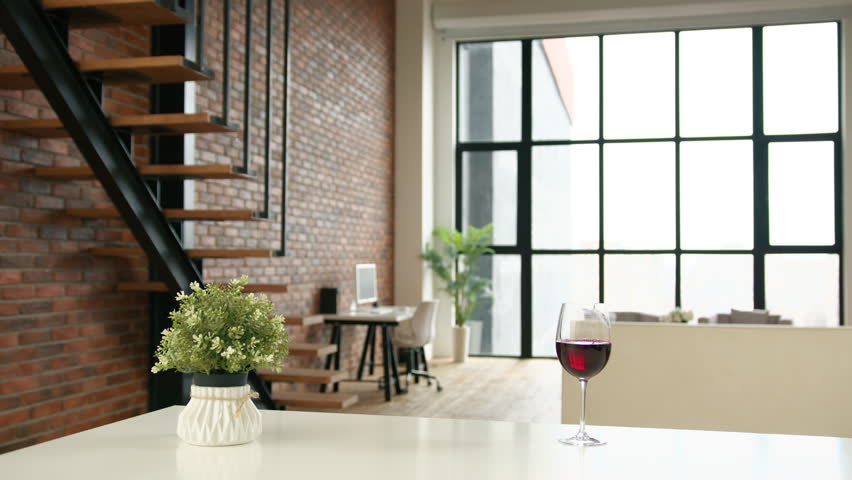 Girl in a white coat and white headphones having fun in a modern loft apartment with large windows. She dances and drinks wine in a pleasant solitary atmosphere. RED 8K RAW