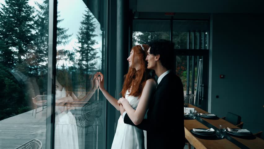 Fairy-tale wedding couple posing in a stylish house with panoramic windows and mountain views. Red-haired bride posing with the groom. Wedding concept Royalty-Free Stock Footage #3405103217