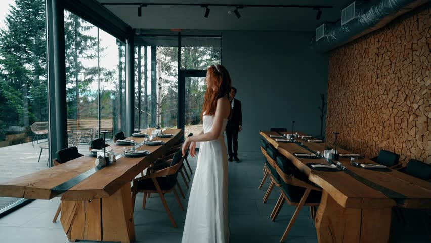 Fairy-tale wedding couple posing in a stylish house with panoramic windows and mountain views. Red-haired bride posing with the groom. Wedding concept Royalty-Free Stock Footage #3405104235