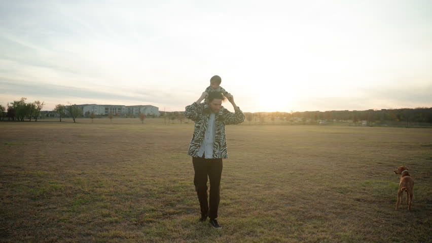 White caucasian dad playing and running in a park with his baby boy on shoulders at sunset. Slow motion Royalty-Free Stock Footage #3405120835
