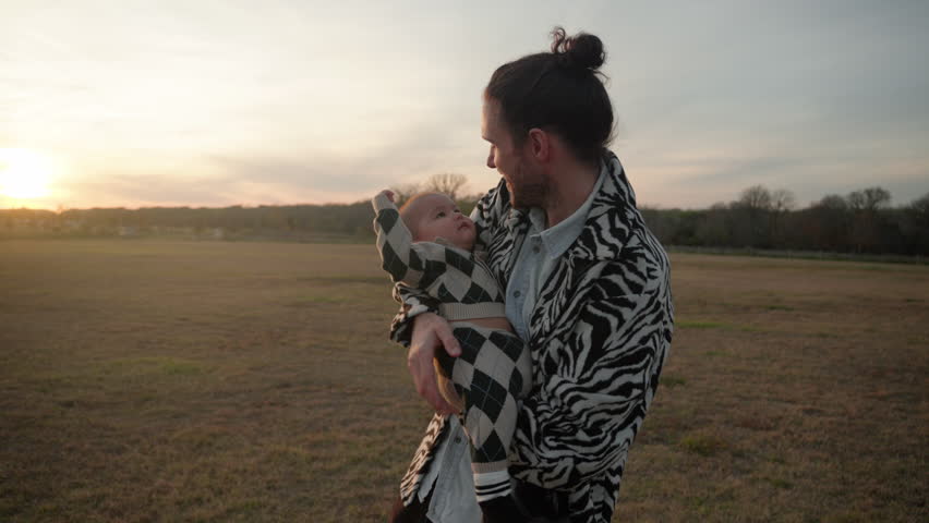 Caucasian white father holding and comforting his infant baby in his arms outdoors in a field at sunset. Slow motion Royalty-Free Stock Footage #3405122477