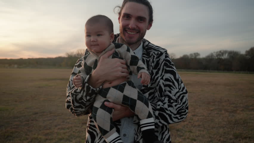 Portrait of white father bouncing his cute baby son outdoors to comfort him and make him happy. Slow motion Royalty-Free Stock Footage #3405122861