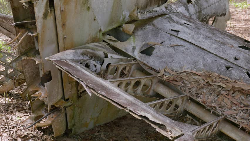 A wrecked Curtiss P-40e Warhawk plane crash in remote far north Australia.  There is a low fence surrounding the spread-out wreckage.  The surrounding thick bushland contrasts the rusted form.  In 4K.