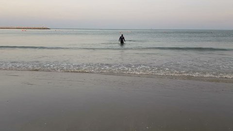 back view of fisherman in blue clothes throwing the net to catch the sea animal or fish at the tropical beach in the evening. man standing in the sea near the shore at dusk.
