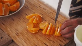 Men's hands cut orange slices on a wooden board. Cooking video