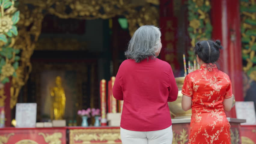 Chinese lunar new year festival and tradition holiday celebration concept. Happy Asian family grandmother and grandchild girl praying a wish with incense and red candle together at Chinese shrine.