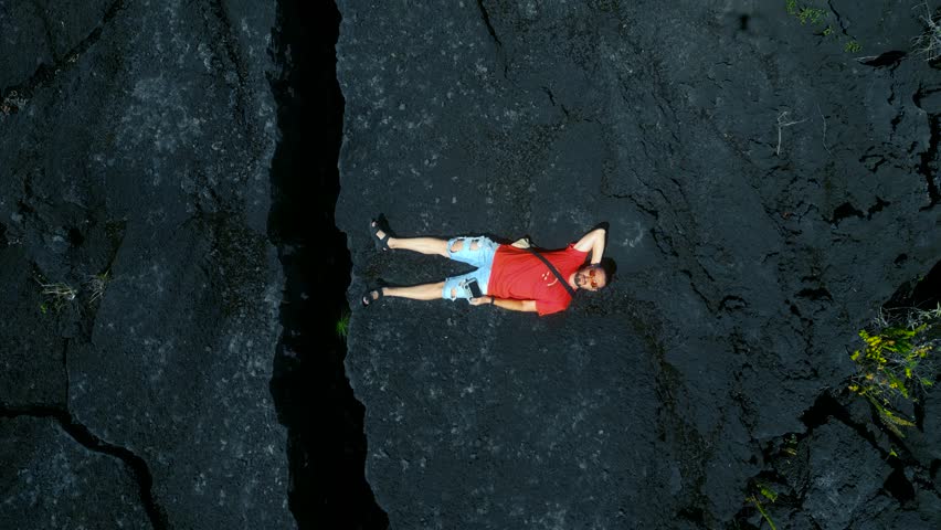 Side view of male photographer in outerwear standing on top of rocky cliff near active volcano Fagradalsfjall with black lava in Iceland in daytime