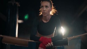 Serious young woman boxer fighter in boxing gloves standing near ropes on boxing ring ready for her fight. Girl thinks about her win. Professional sport, competition. Female power concept. - Powered by Shutterstock - Get 15% off with code: PIKWIZARD15