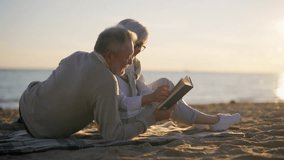 Senior gray haired man woman reading book together sitting on sandy sea beach at sunset in evening. Happy marriage, old family spending enjoy time. Love couple relationship, leisure, resting concept. - Powered by Shutterstock - Get 15% off with code: PIKWIZARD15