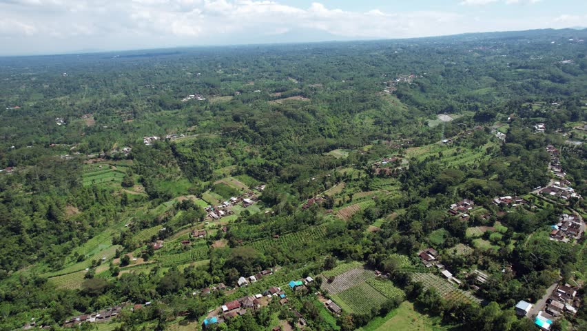 Many small villages scattered around green forested landscape at side of old volcano, aerial shot of Bali Island near Batur. Roads and farmland seen here and there, volcanic terrain with many ravines