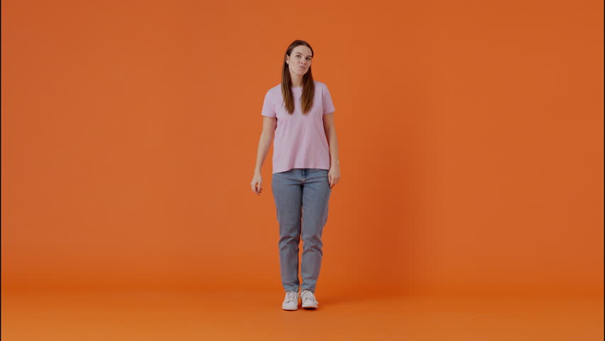 Brunette woman in t-shirt and jeans dancing energetically and waving hands and body amusingly in orange studio. Caucasian female partying alone and enjoying rhythmic movements for spirit lifting. Royalty-Free Stock Footage #3405483343