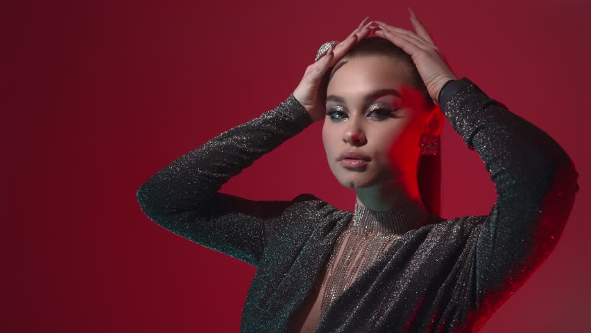 A young seductive fashion model girl with bright evening makeup and stylish hairstyle shows off jewelry with precious stones, poses and looks at the camera in the light of red lanterns.