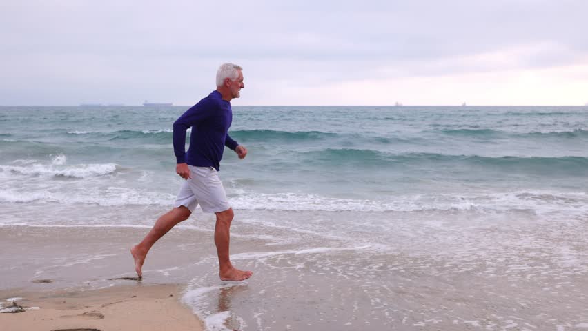A mature 66 year old man jogging at the beach in Southern California. Slow Motion.