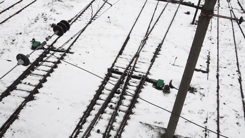 aerial view of railway tracks during winter, with snow covering the ground. Multiple tracks intersect and diverge, indicating a switching area for trains. 
