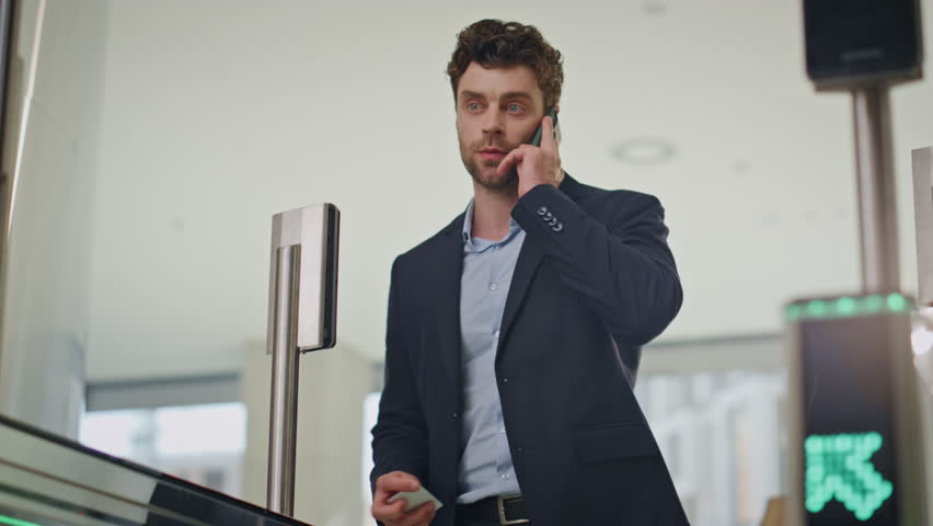 Office manager walking through checkpoint corporate security talking cellphone. Rich company employee swiping card entering in turnstile. Elegant businessman passing electronic gates business center.