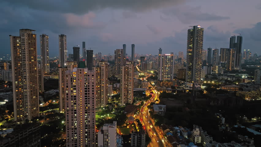 An aerial view of Mumbai's high-rise buildings and beautiful nightlights. The sky is cloudy, and there is medium traffic on the road. The cityscape is filled with modern illuminated buildings. Royalty-Free Stock Footage #3405674623