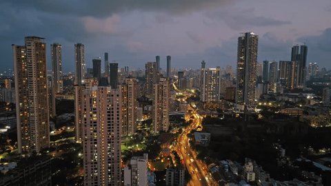 An aerial view of Mumbai's high-rise buildings and beautiful nightlights. The sky is cloudy, and there is medium traffic on the road. The cityscape is filled with modern illuminated buildings.: stockvideo